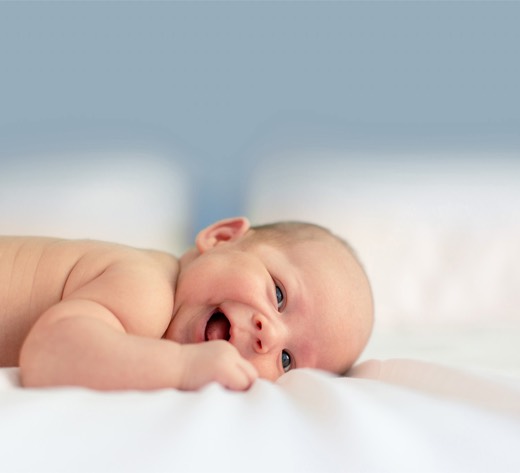 Lachendes Baby in Bauchlage auf einer weißen Decke